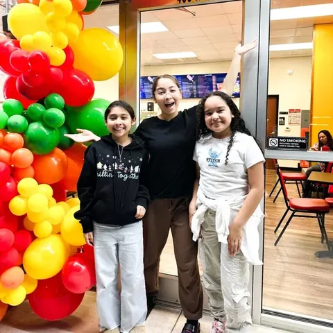 Three friends posing under the balloon arch at the Chicos door