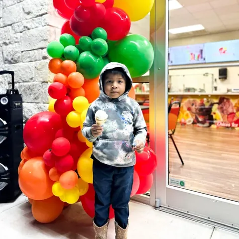 A little boy in a hoodie holding a cone in front of the balloon arch
