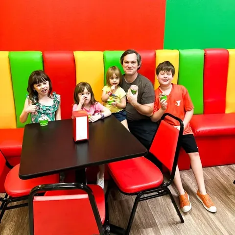 A dad and four kids with ice cream cups in the striped booths