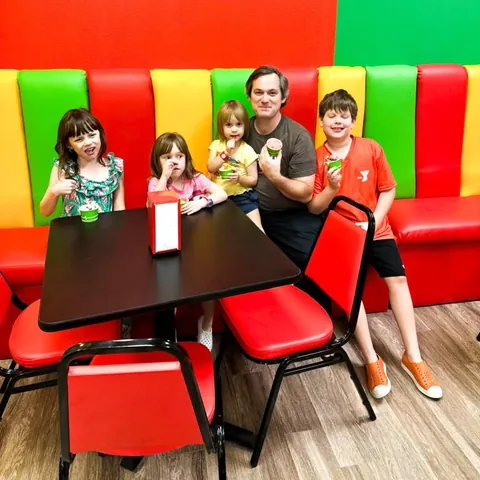 A dad and four kids holding ice cream cups against the red wall